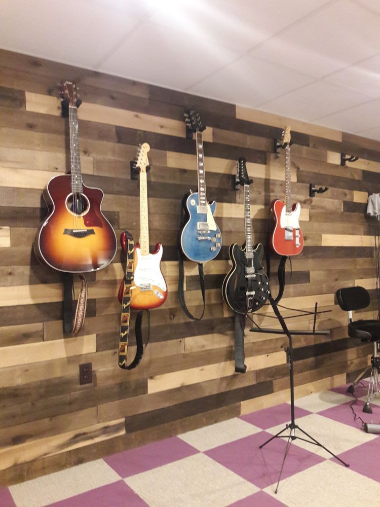 A bunch of guitars are hanging on a wooden wall