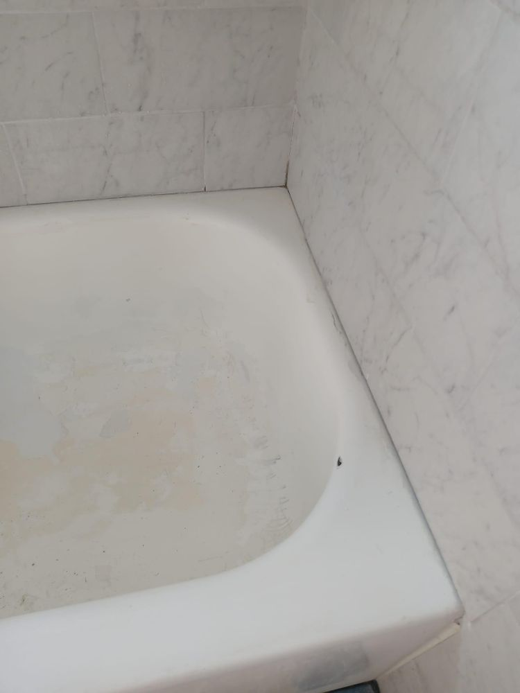 A white bathtub is sitting in a corner of a bathroom next to a marble wall