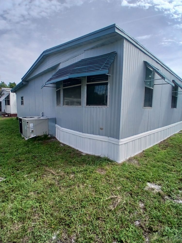 A mobile home with a blue awning is sitting on top of a lush green field