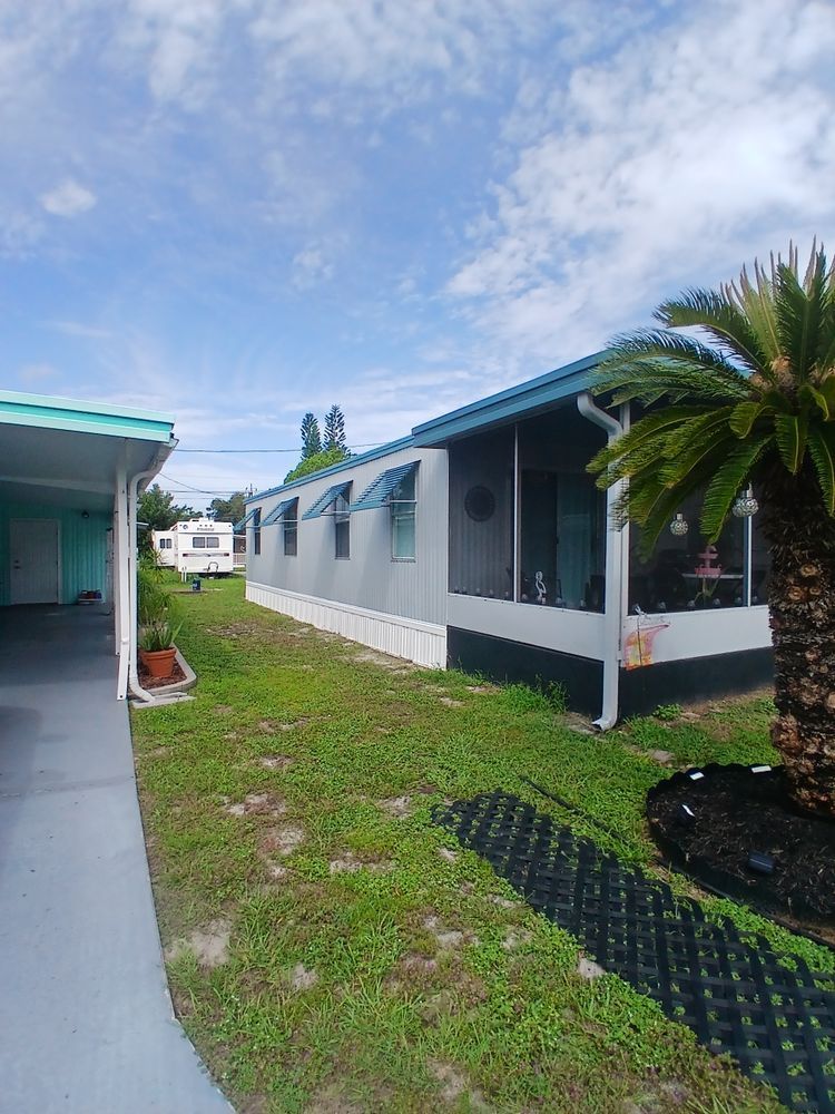 A mobile home with a screened in porch and a palm tree in front of it.