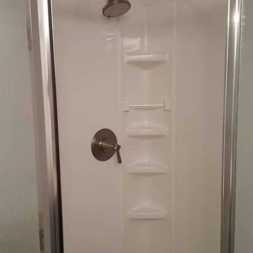 A shower stall with a shower head and shelves in a bathroom