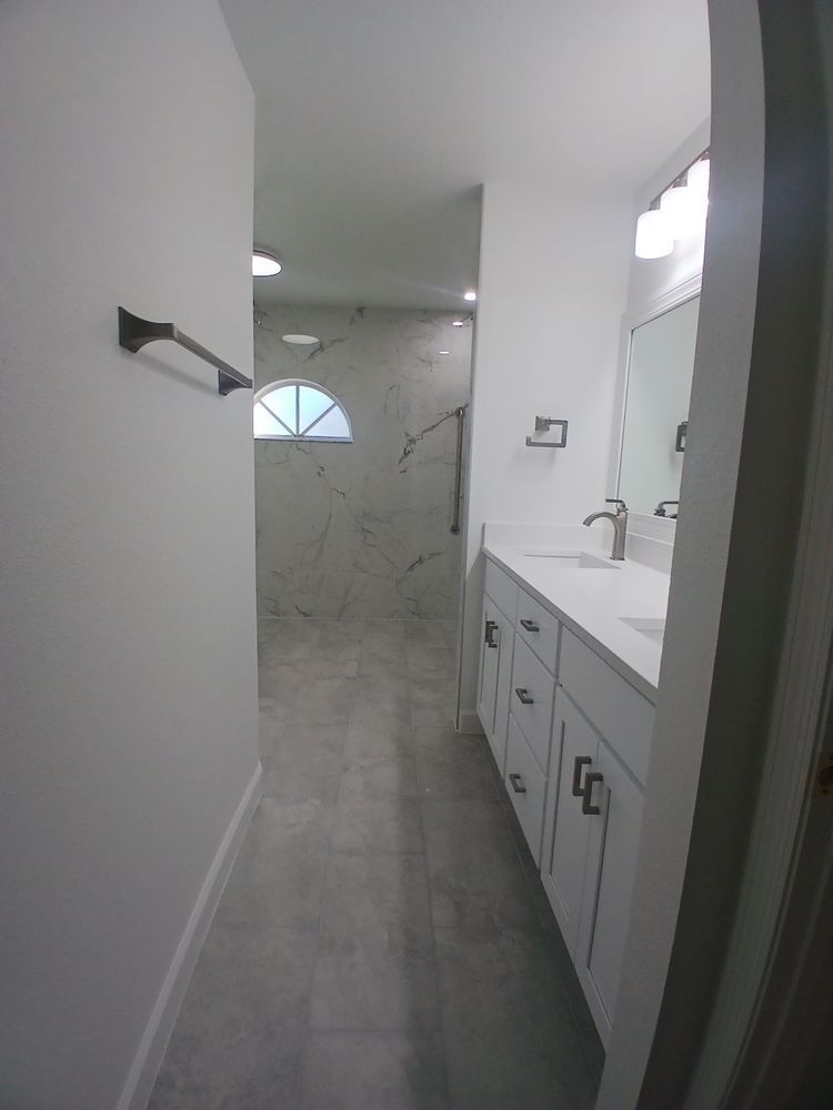 A bathroom with white cabinets , a sink, a mirror and a walk in shower