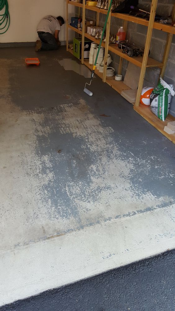 A man is kneeling down in a garage painting the floor.