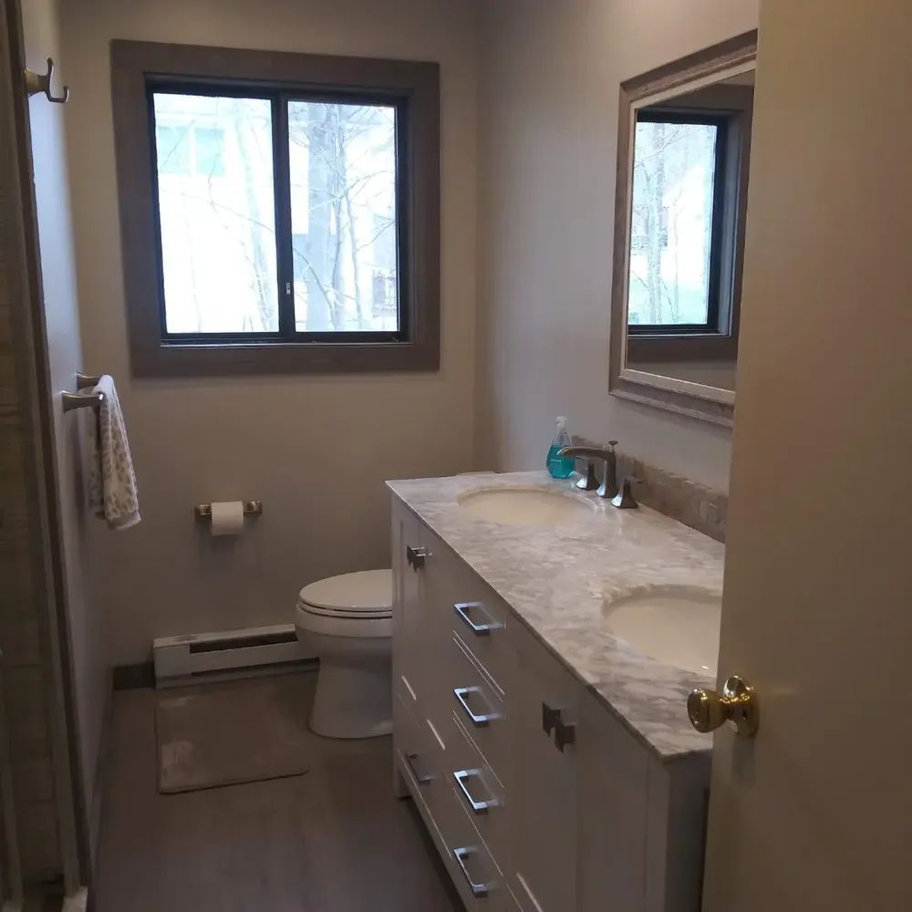 A bathroom with a toilet, sink, mirror and window