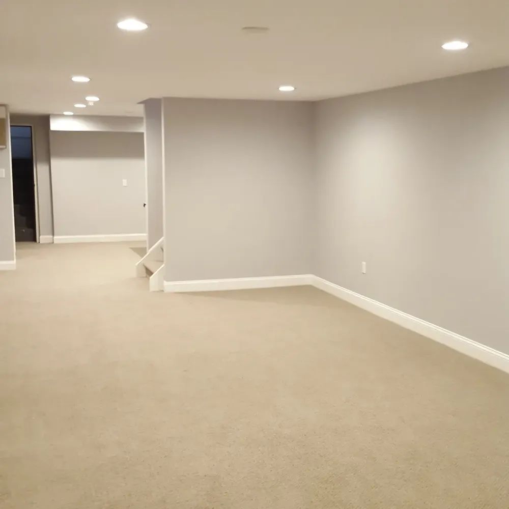 An empty basement with tan carpet and white trim