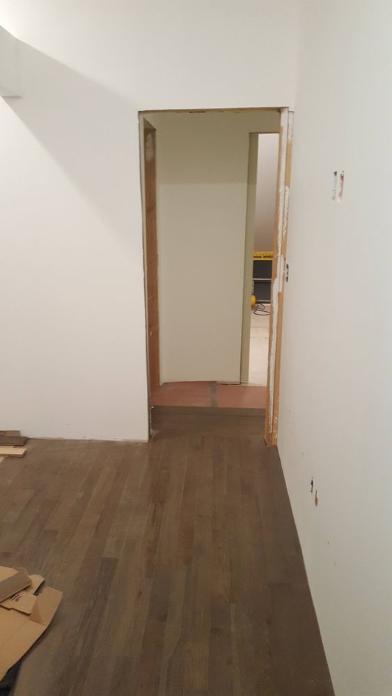 A hallway with a wooden floor and a white wall.