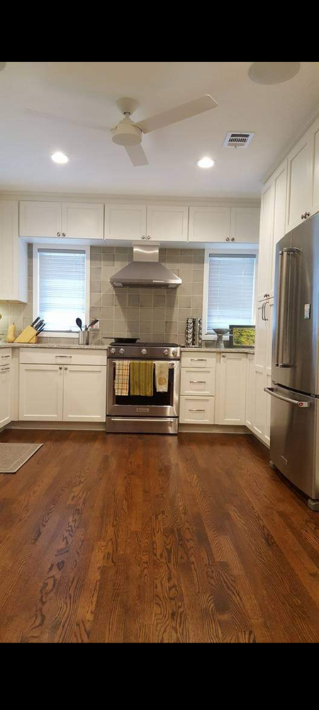 A kitchen with white cabinets , stainless steel appliances, hardwood floors and a ceiling fan