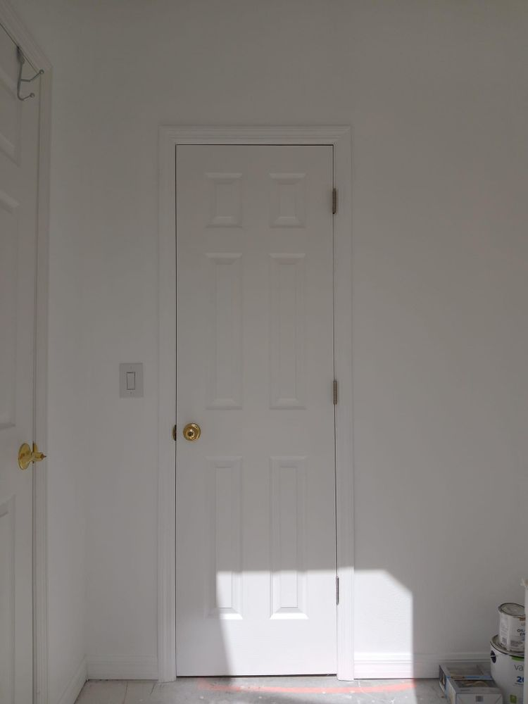 A white door is in a room with white walls