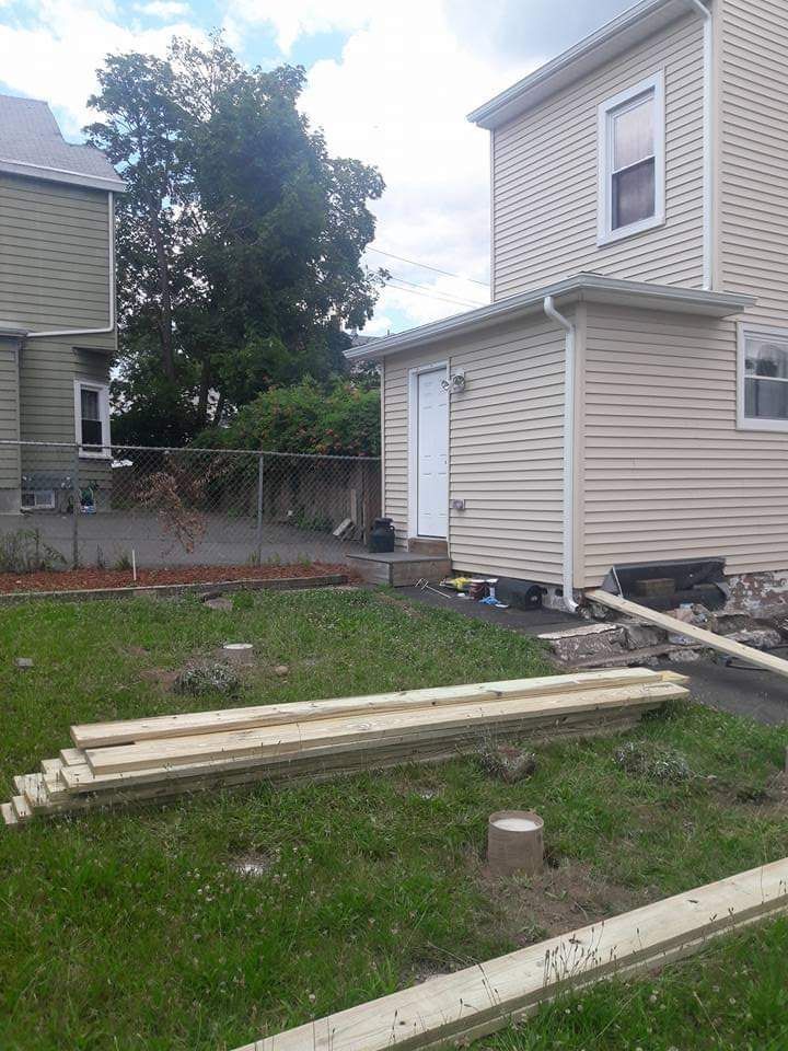 A stack of wood is sitting in the grass in front of a house.