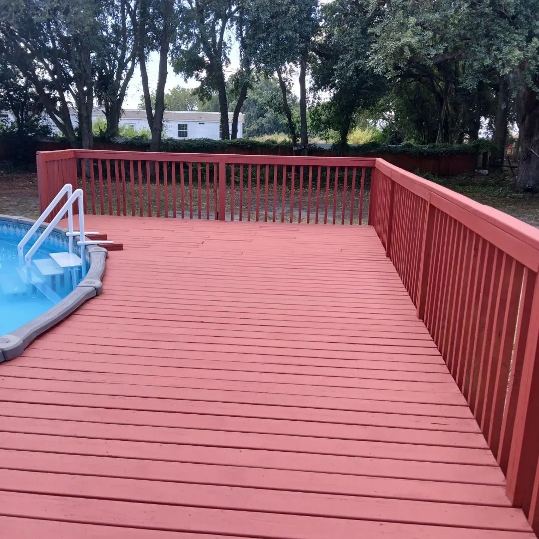 A red deck next to a swimming pool with stairs leading to it.