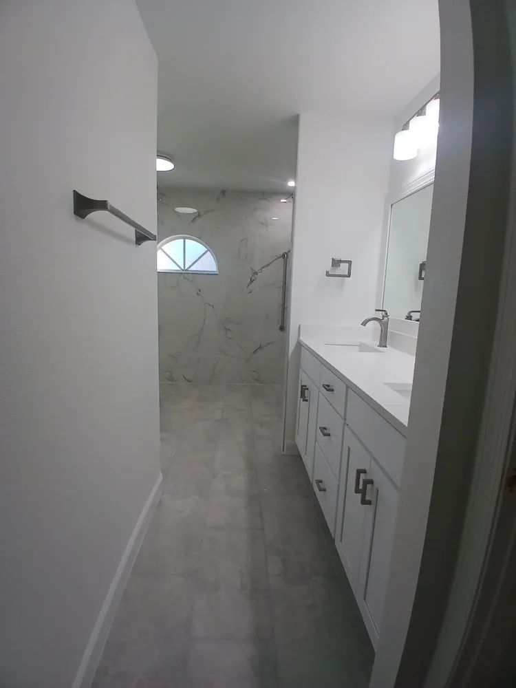 A bathroom with white cabinets, a sink, a mirror and a walk in shower