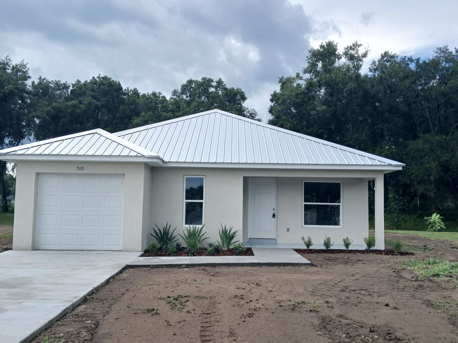 A white house with a metal roof and a concrete driveway
