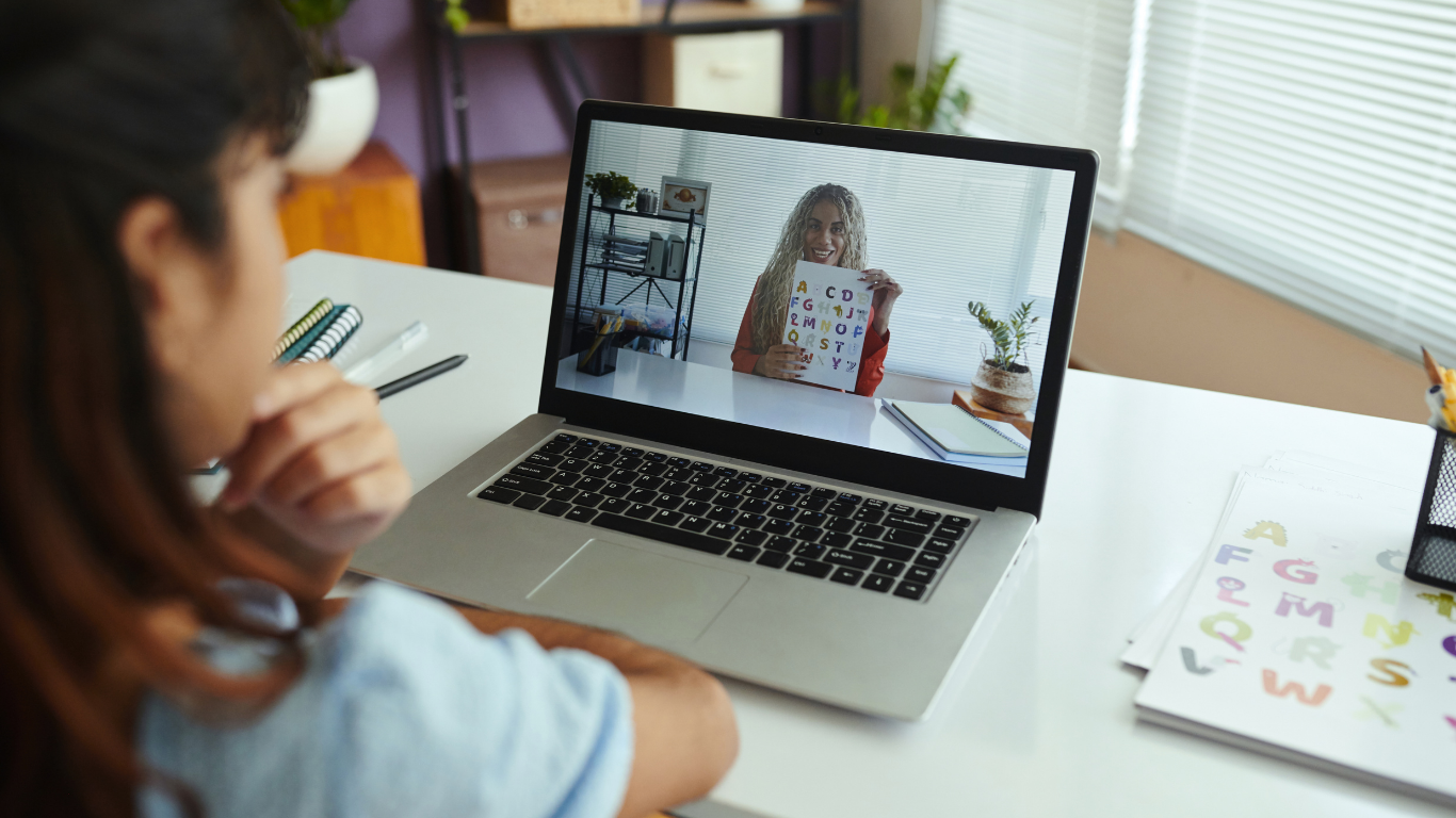 Student watches teacher on laptop screen during virtual lesson.