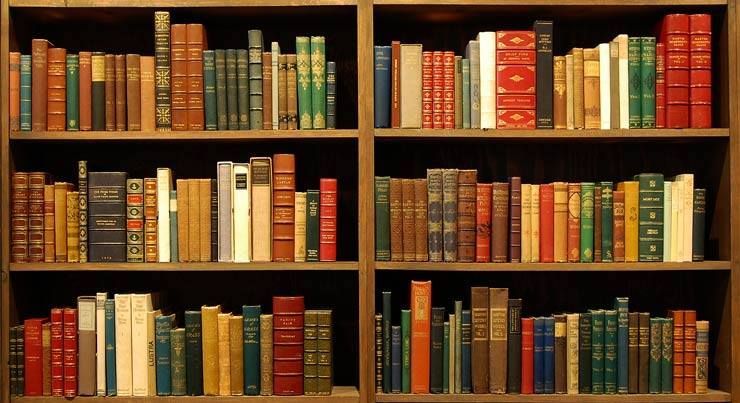 A wooden bookshelf with three tiers, packed with numerous old, colorful hardcover books organized in rows.