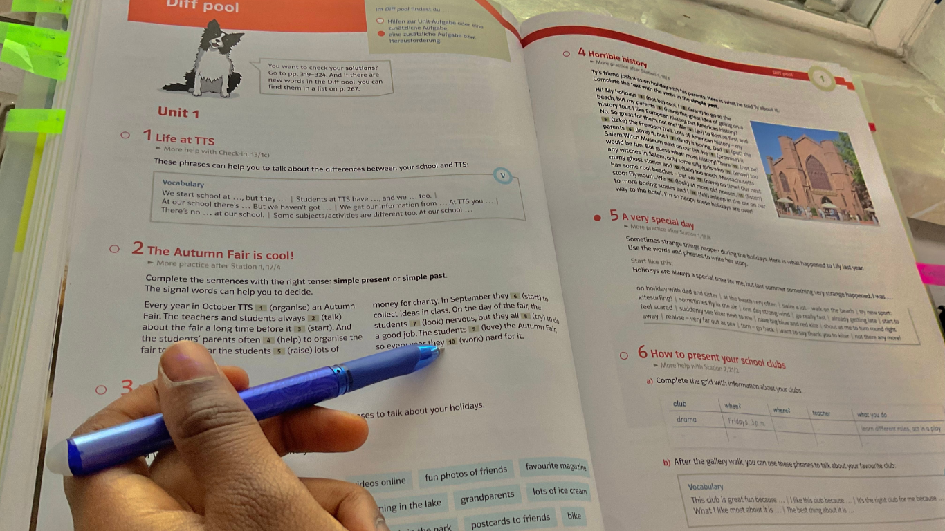 Open textbook with notes, hand holding a blue pen pointing at text.