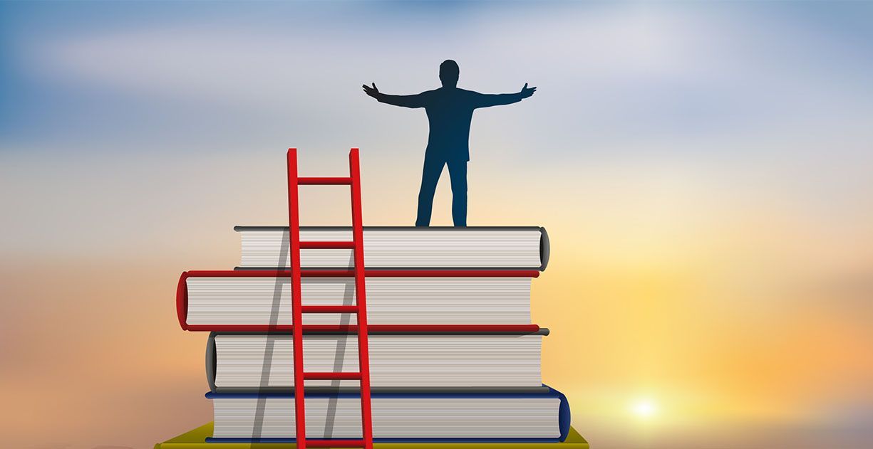 A silhouette of a person standing with arms outstretched atop a stack of books next to a red ladder against a sunset.