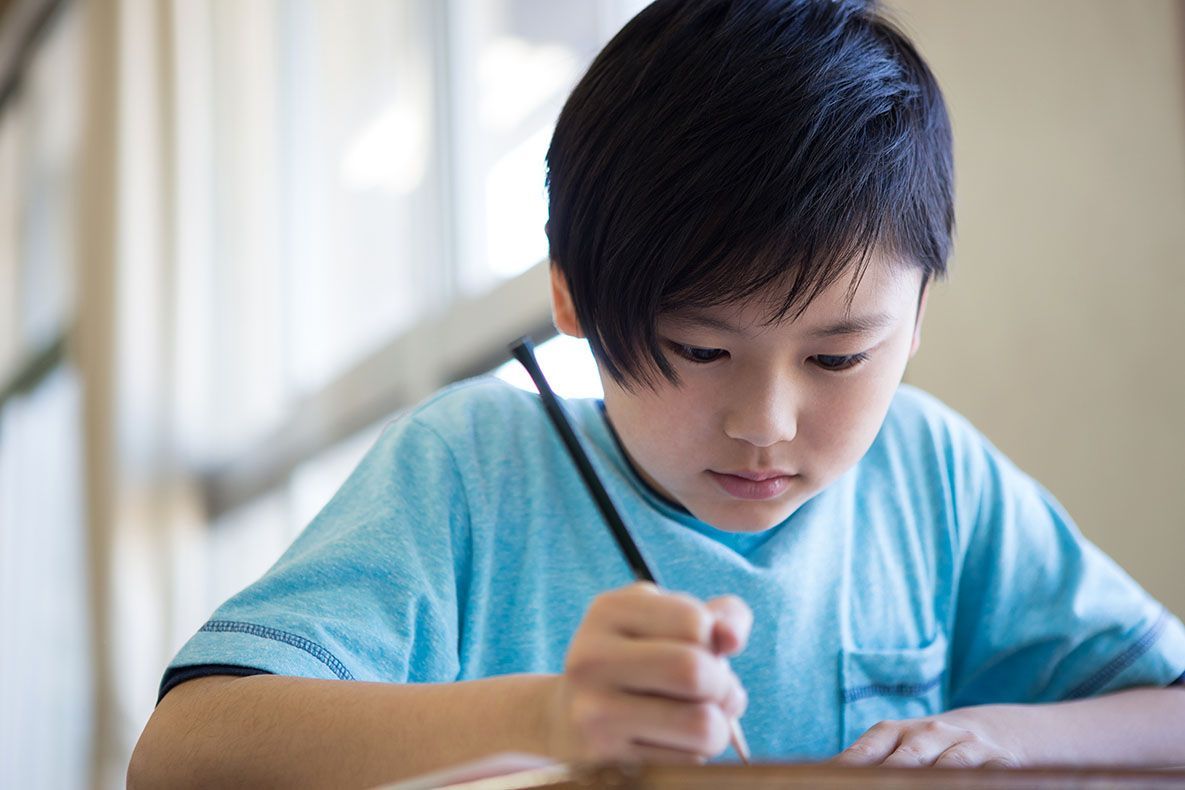 A student in a light blue shirt focused on writing in a notebook.