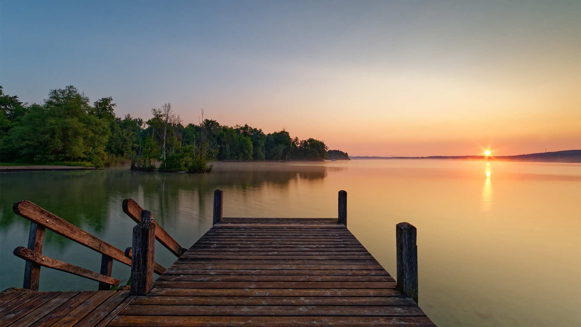 Steg am See beim Sonnenuntergang umgeben mit Schilf