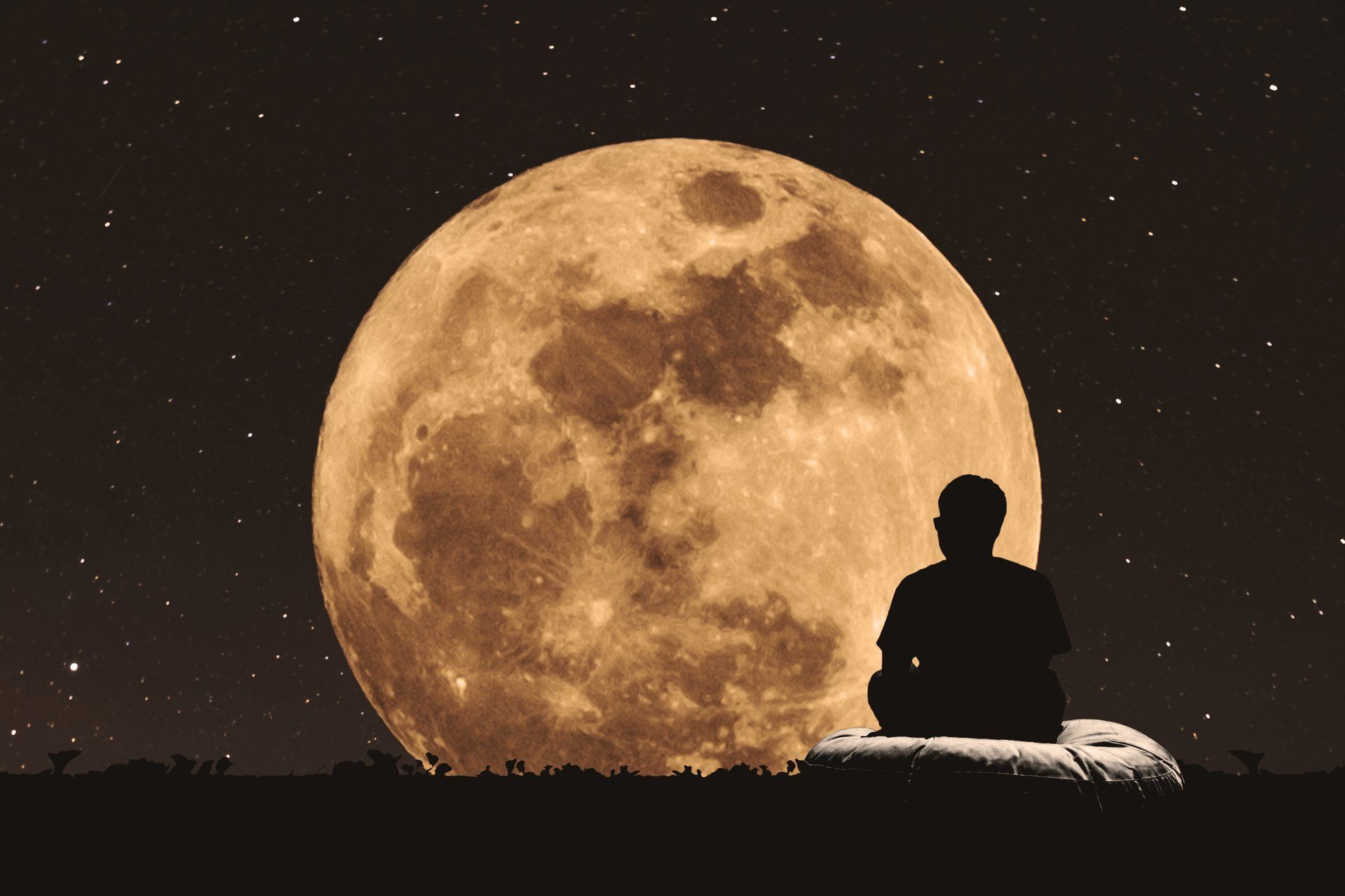 Mann sitzt auf Wiese und betrachtet Sternenhimmel mit Mond
