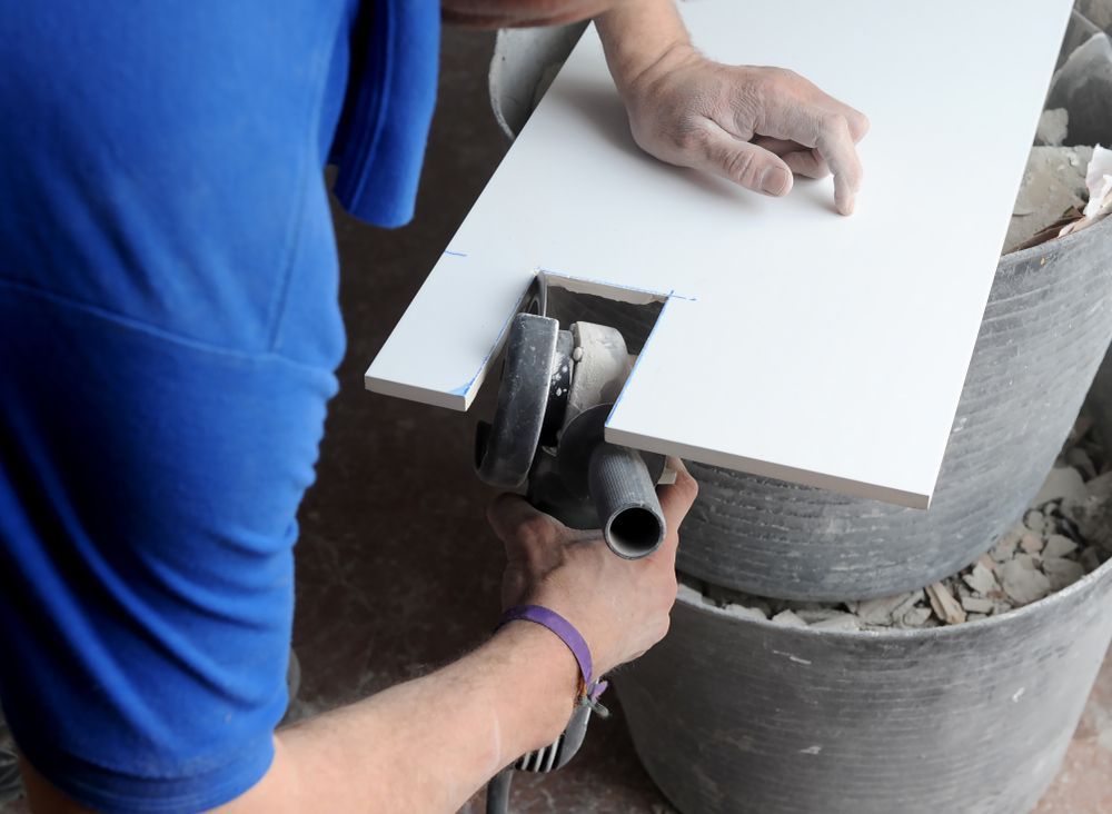 A Man In A Blue Shirt Is Cutting A Tile With A Machine — Tile Power Dubbo In Dubbo, NSW