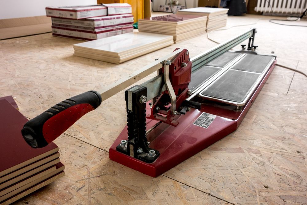 A Tile Cutter Is Sitting On A Wooden Floor Next To A Stack Of Tiles — Tile Power Dubbo In Dubbo, NSW