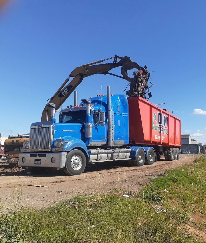 Metal scrap being loaded into an orange bin on the back of a blue truck.