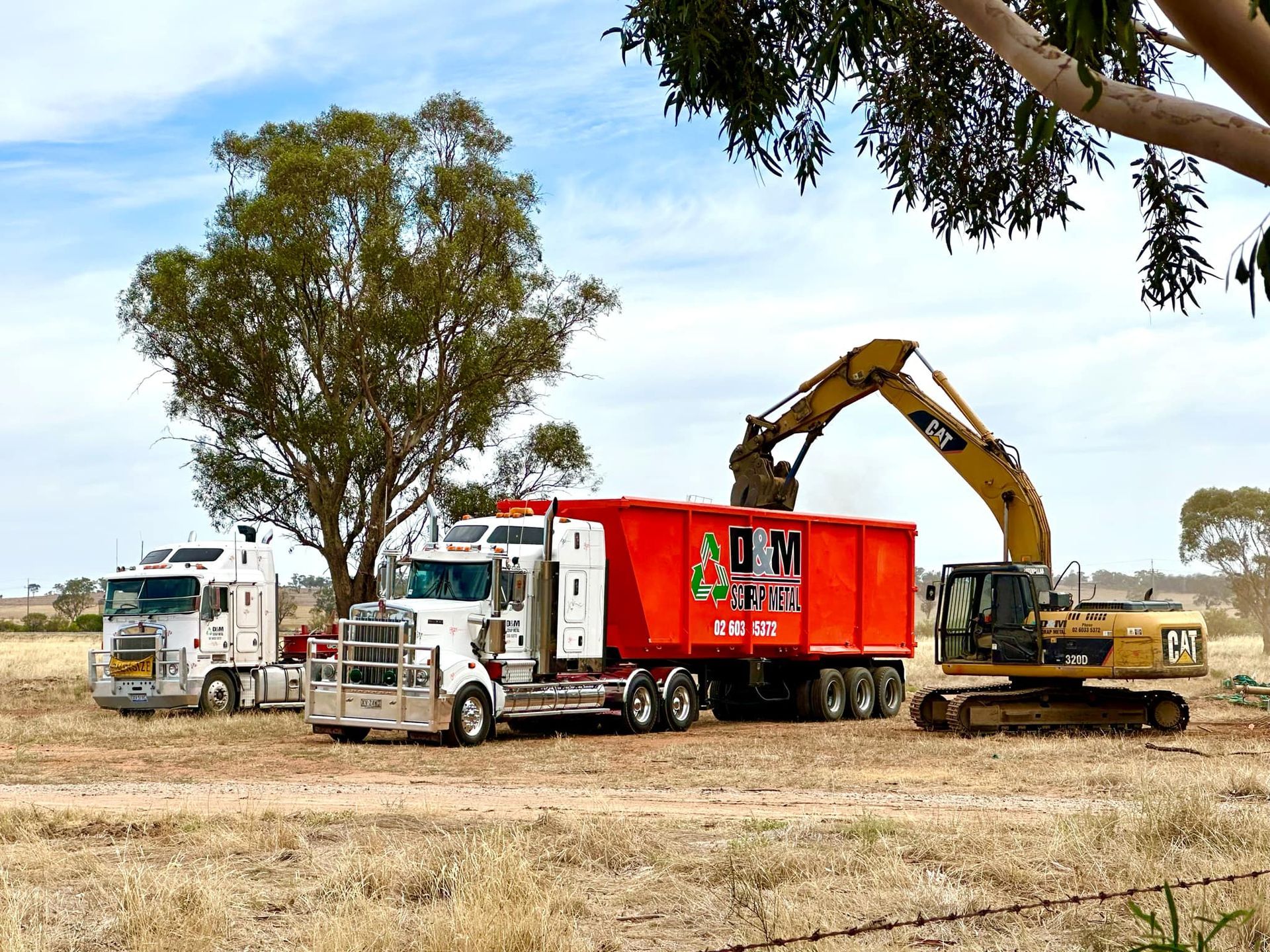A yellow excavator loading scrap metal onto the back of a truck in a orange bin.