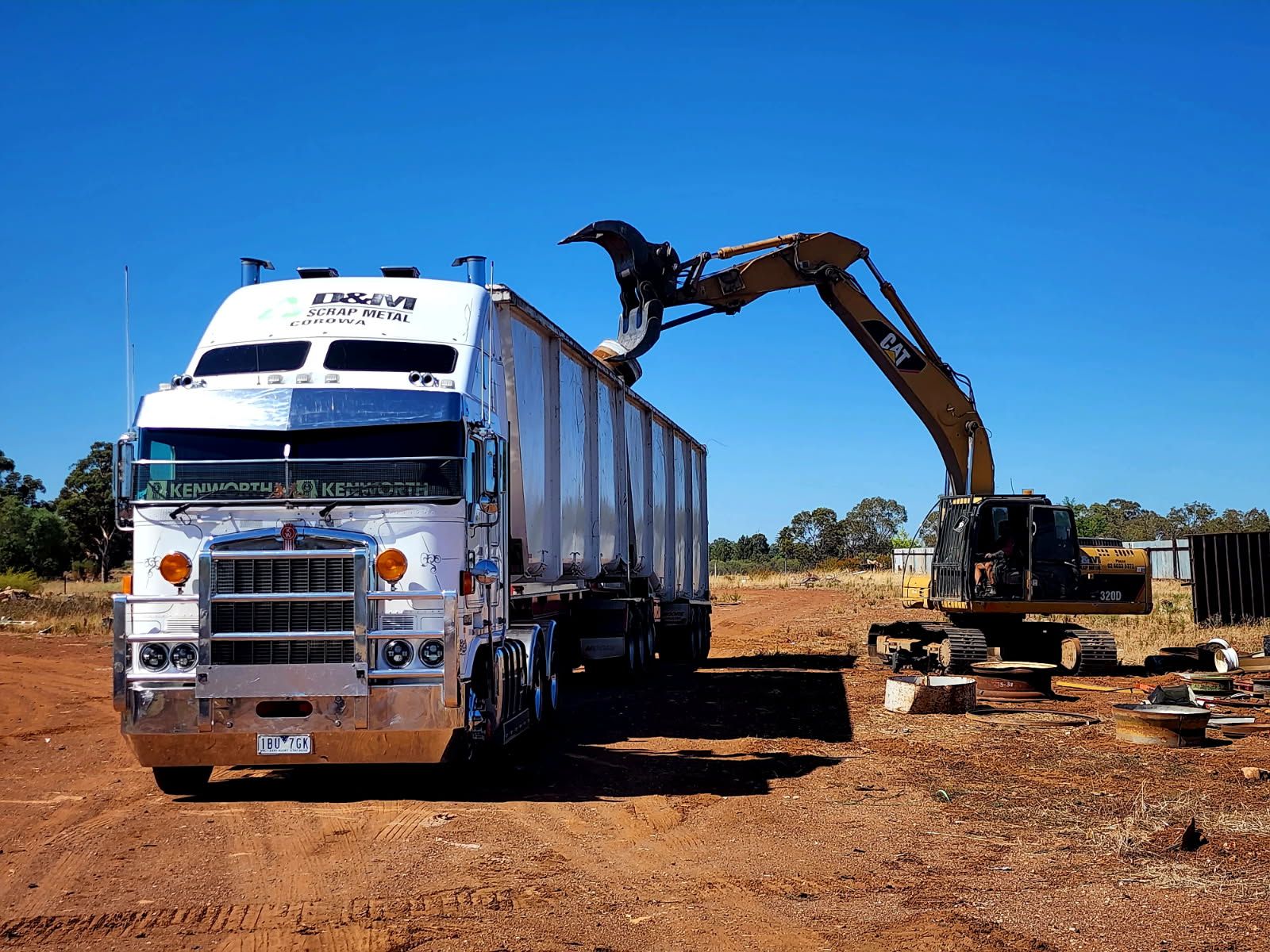 A yellow excavator with a claw loading scrap into a white truck.