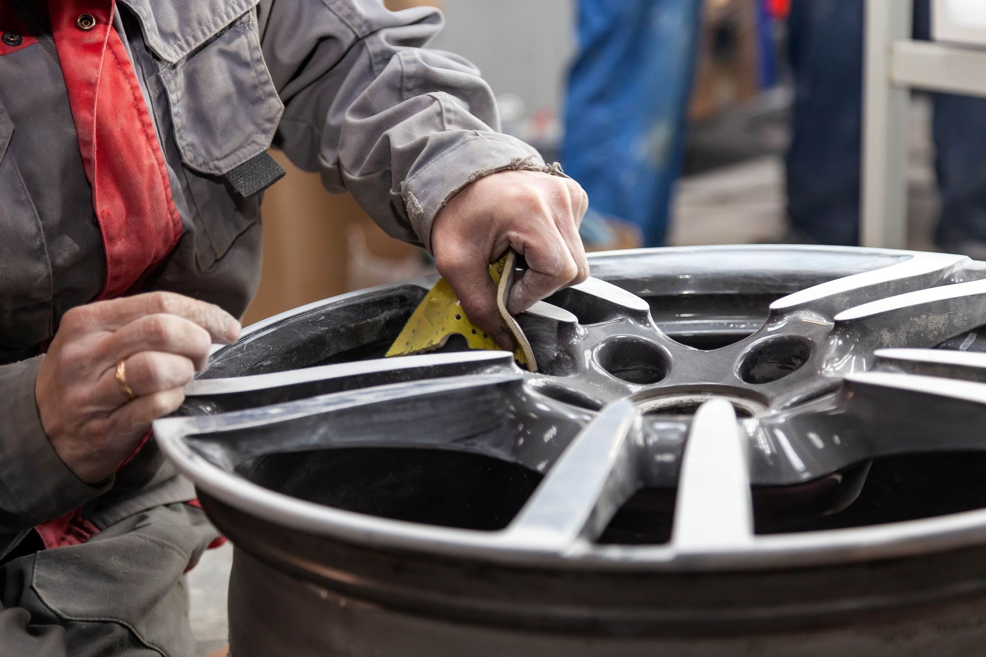 Person sanding the surface of a car wheel in a workshop.