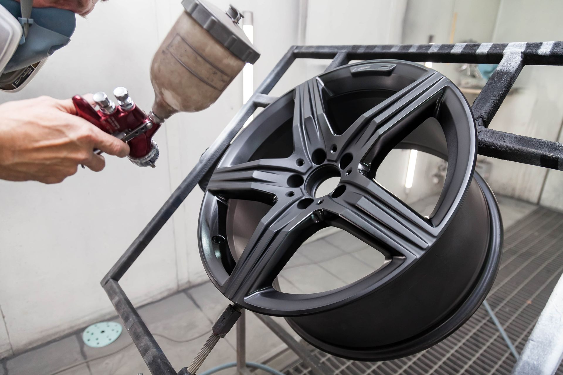 Person spraying paint on a black car wheel in a workshop.