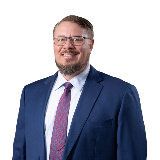 Man in a blue suit, glasses, and a patterned tie, smiling. Studio shot.