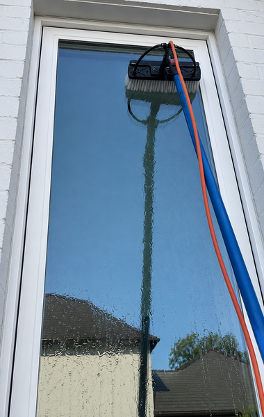 Window cleaning tool on a tall glass window, with blue and red hoses attached.