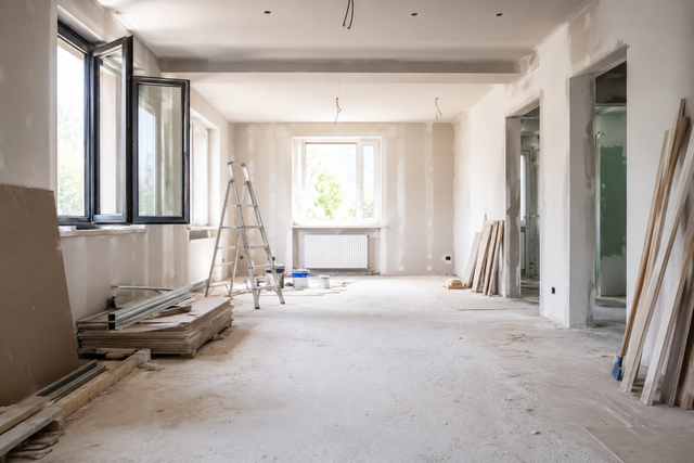 Bright unfinished room with open windows, ladder, and building materials during renovation.