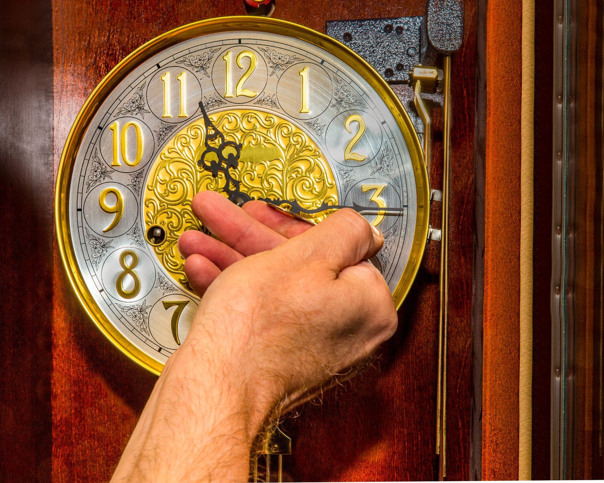 A man's hand winding a grandfather clock