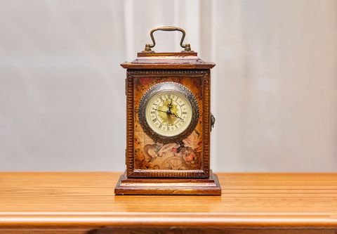 Ornate vintage clock on a wooden table against a plain gray background.