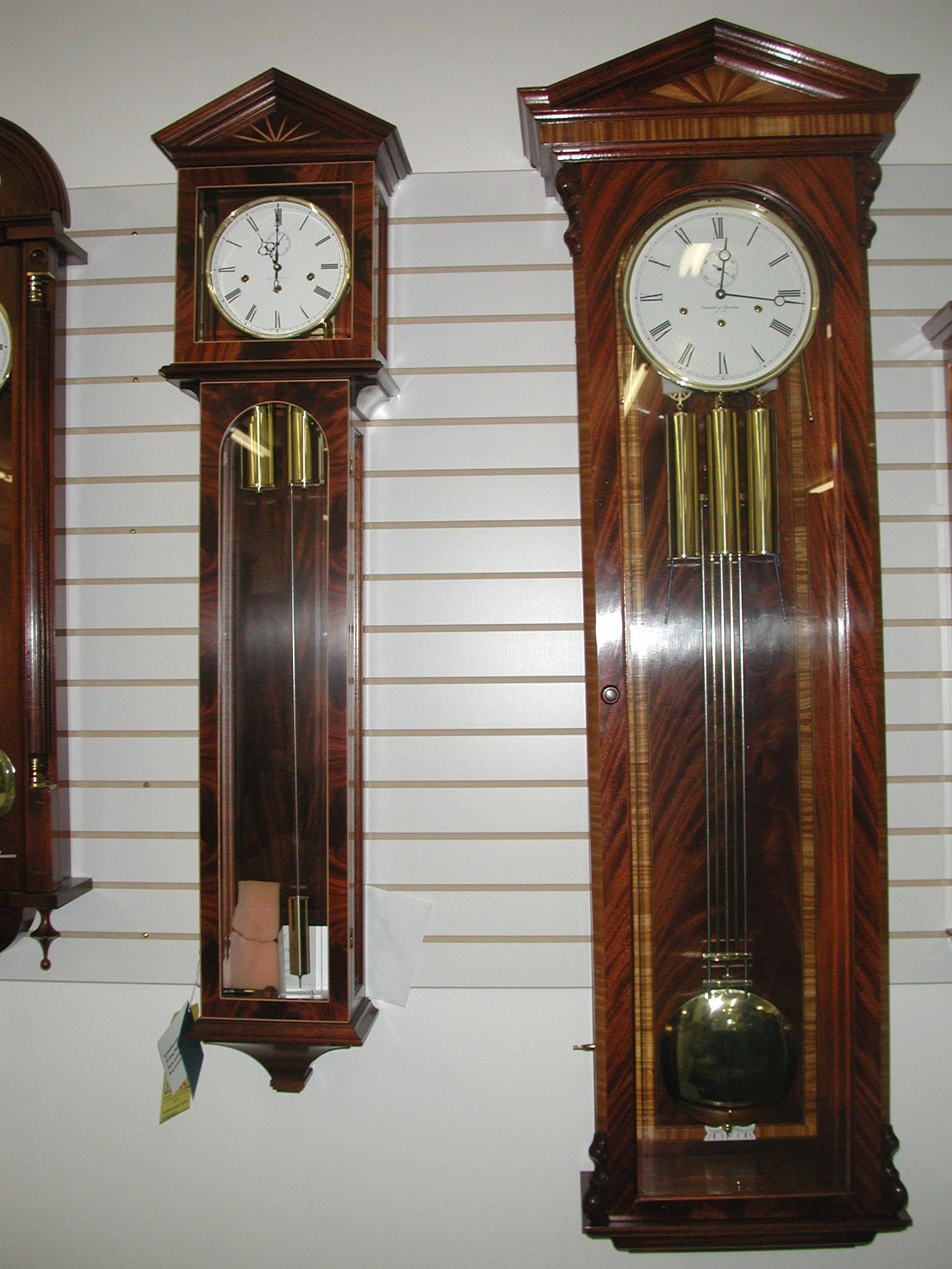 Two dark wooden grandfather clocks on a white-striped wall.