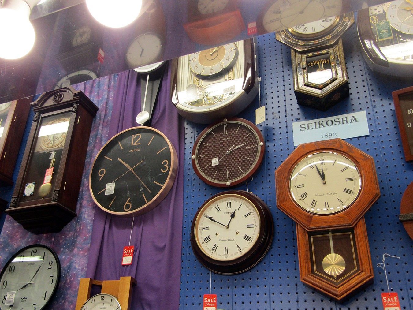 Variety of clocks displayed on a wall. Brown, black, and white faces, different shapes and sizes.