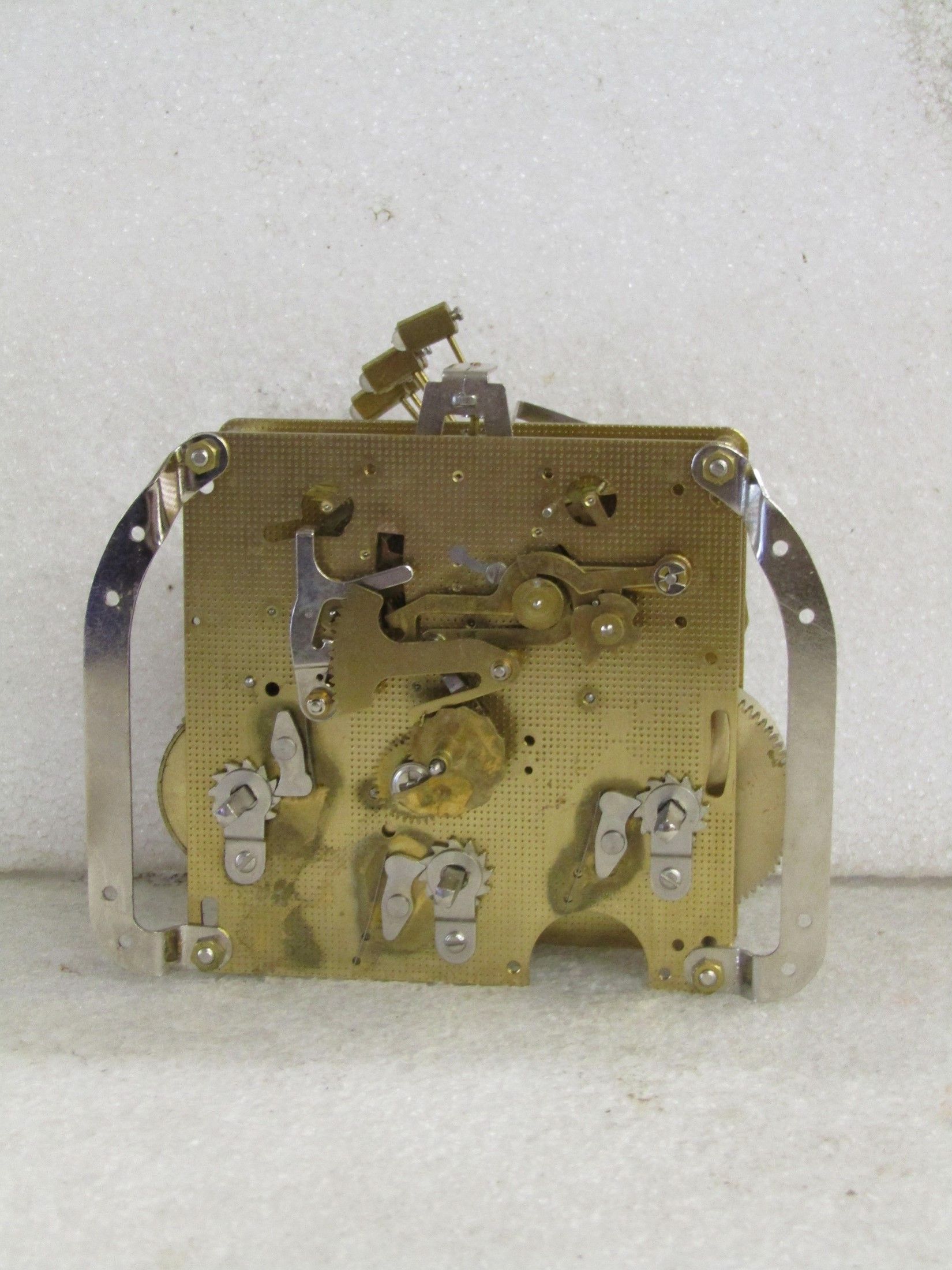 Clock mechanism with gold-colored gears and metal arcs, viewed from the back.