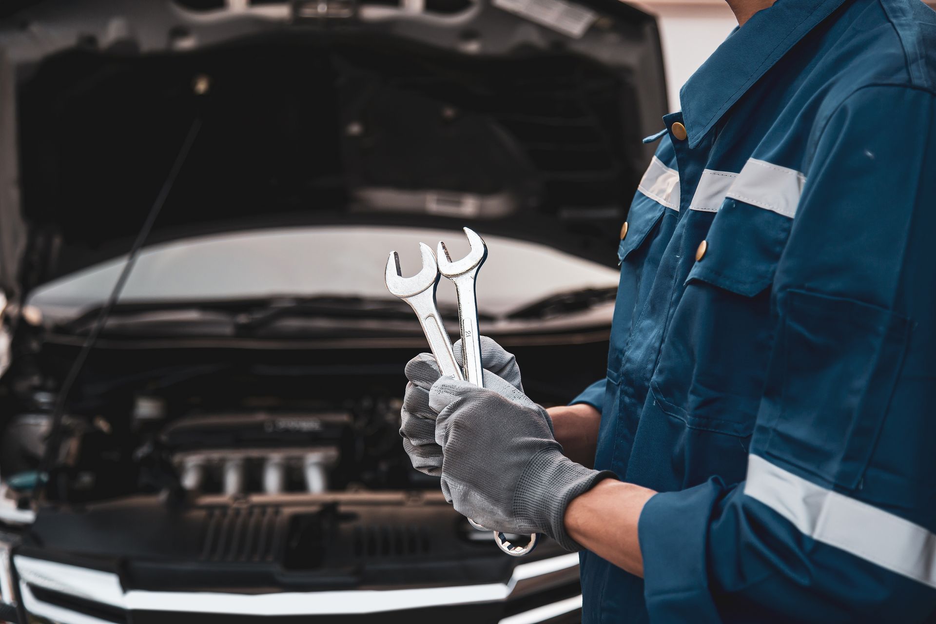 A mechanic is holding two wrenches in front of a car.