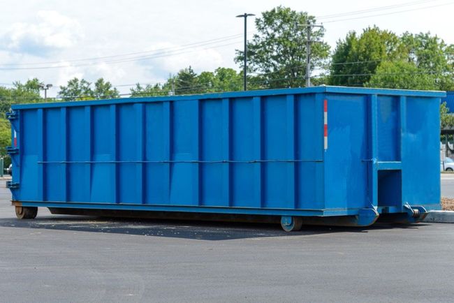 Blue dumpster on wheels in a paved area, parked outside.