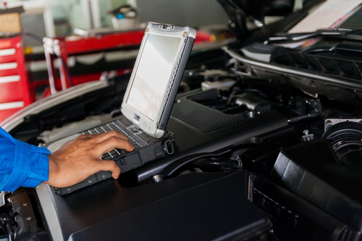 A person is using a laptop computer under the hood of a car - AK Auto Repair