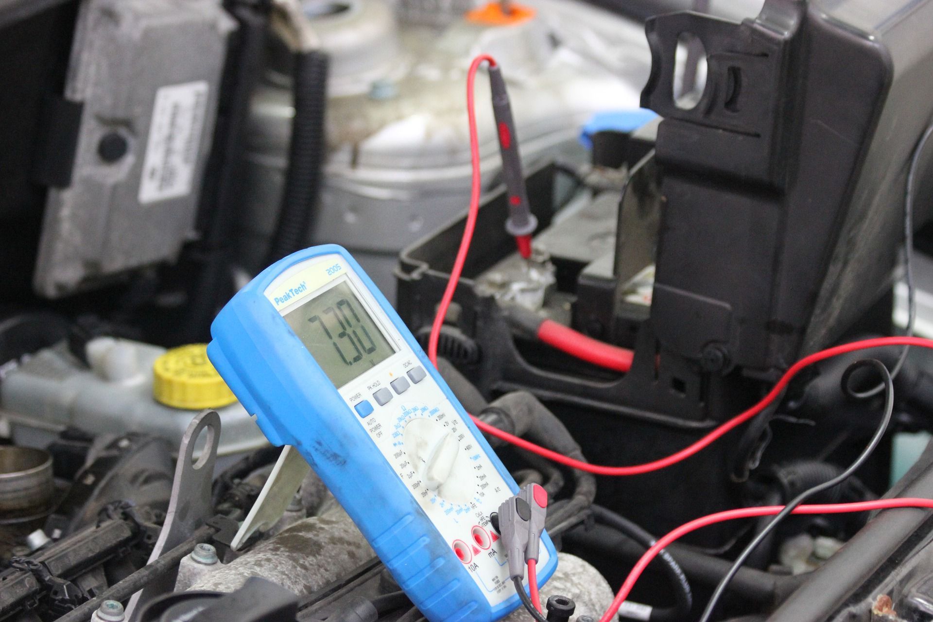A multimeter is sitting on top of a car engine - AK Auto Repair