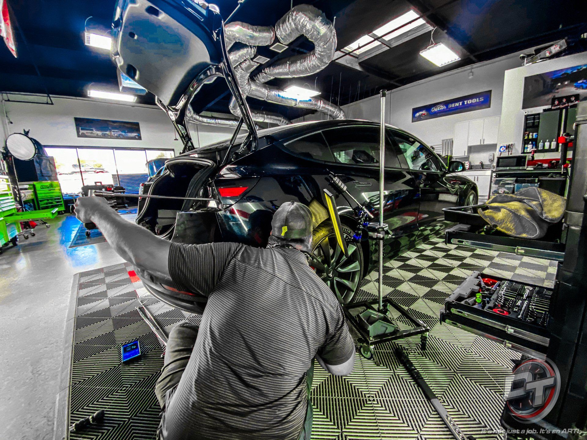 A man is working on a car in a garage with the trunk open.