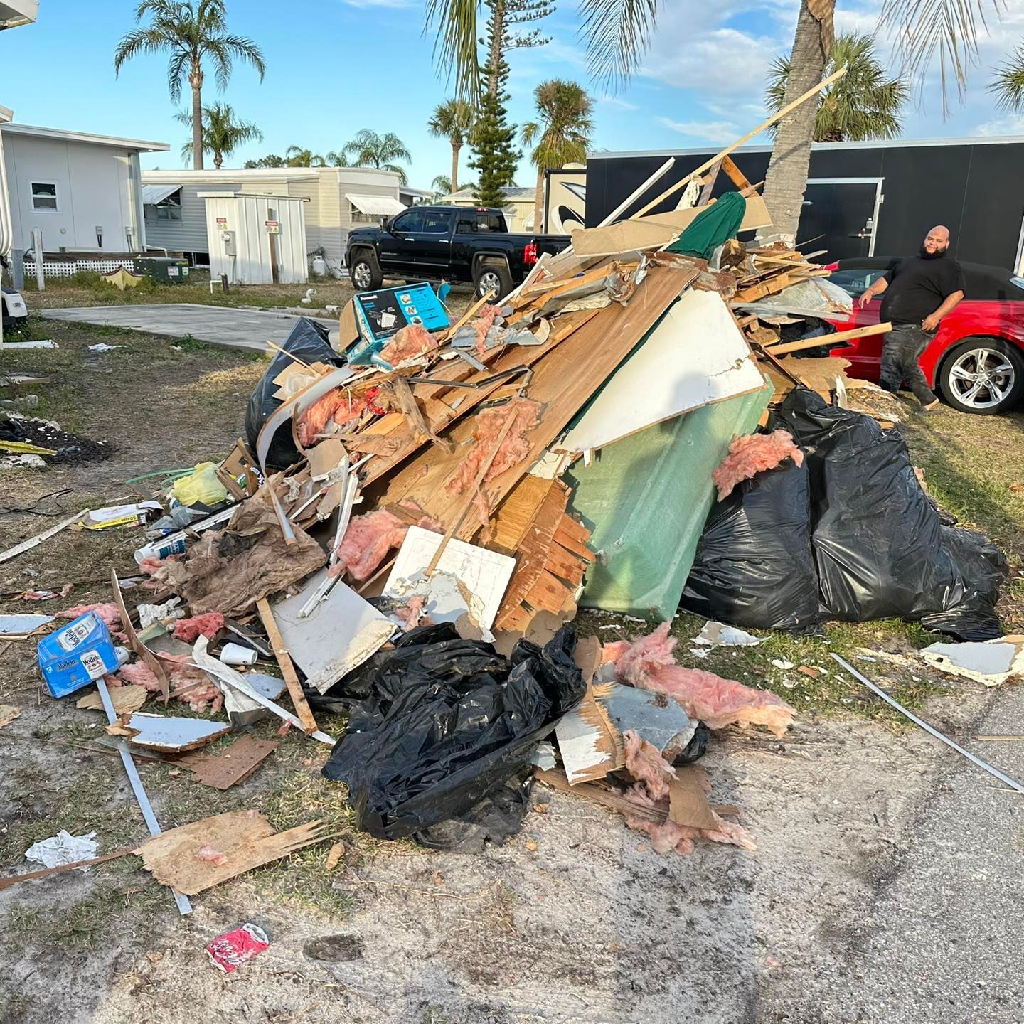 Pile of debris and trash on a driveway, next to a black car and a person.