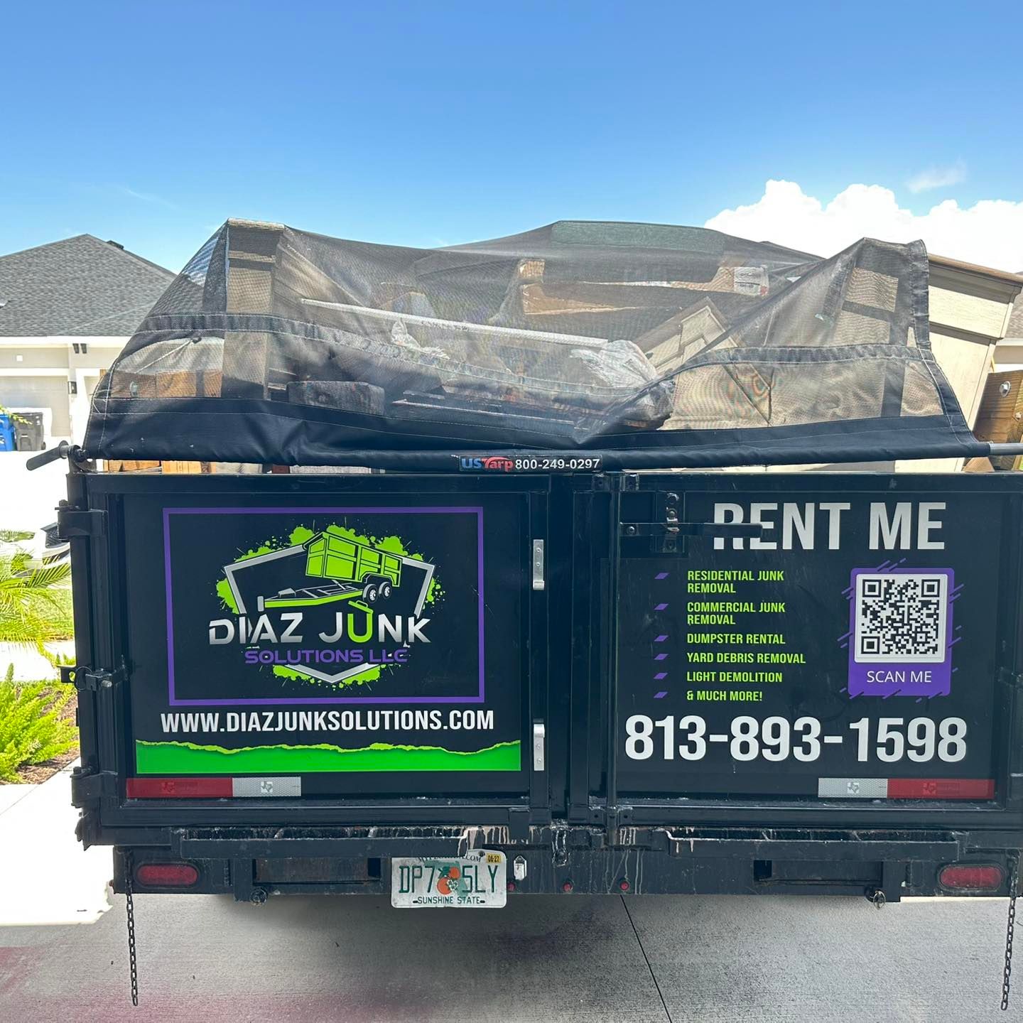 Diaz Junk Solutions truck loaded with debris, black with green and purple logo, parked outdoors. 
