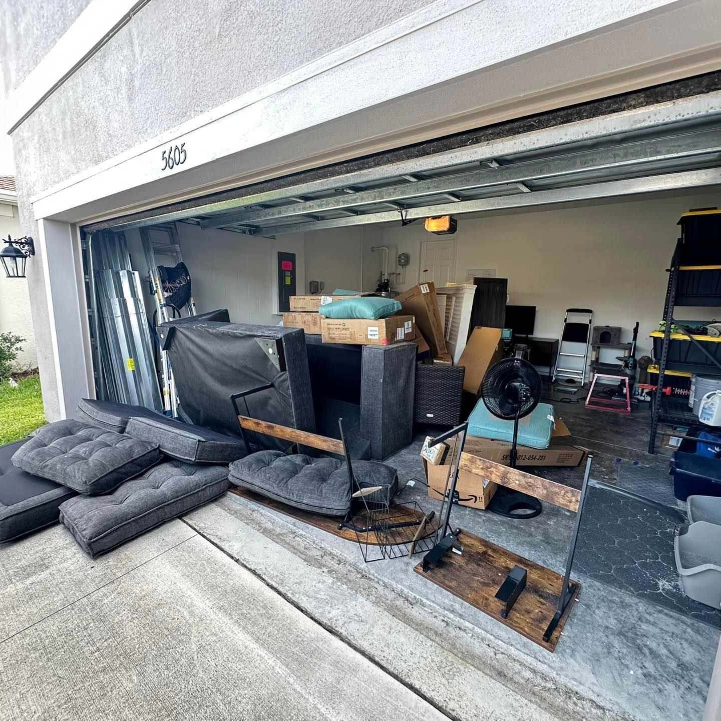 Garage filled with furniture, boxes, and other items. Some items are outside the garage.