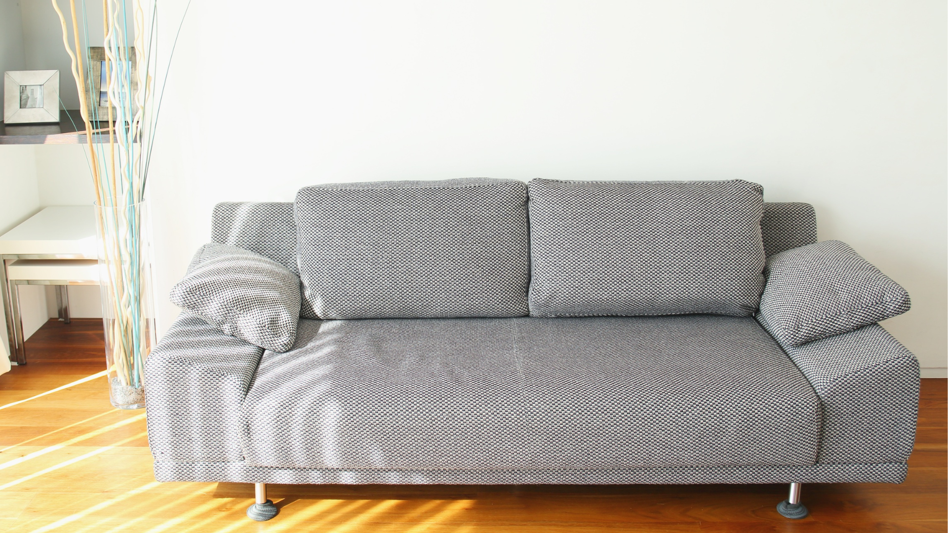 Gray patterned couch against a white wall in a sunlit room.