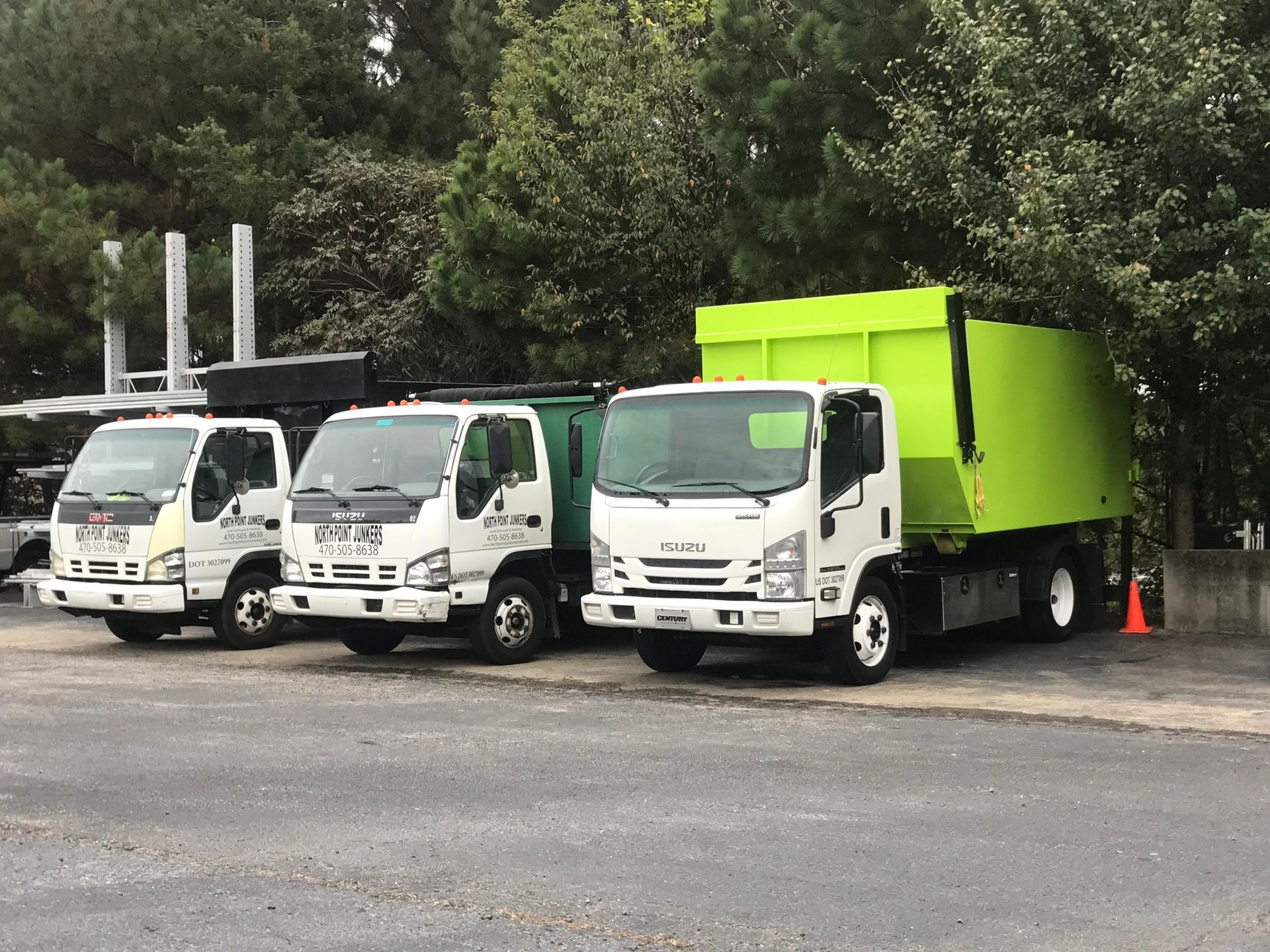 Three garbage trucks are parked next to each other in a parking lot.