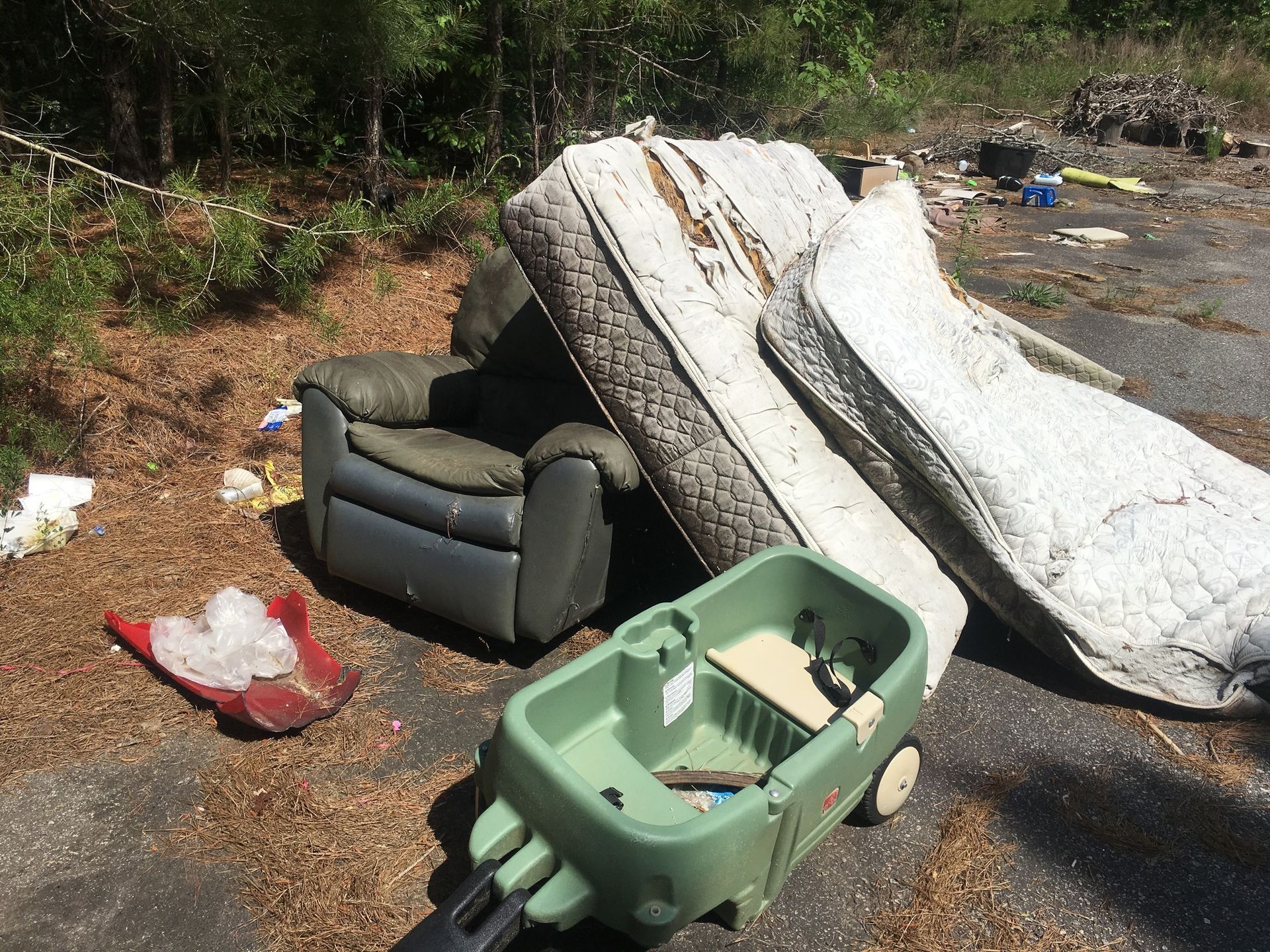 A green wagon is pulled by a mattress and a chair.
