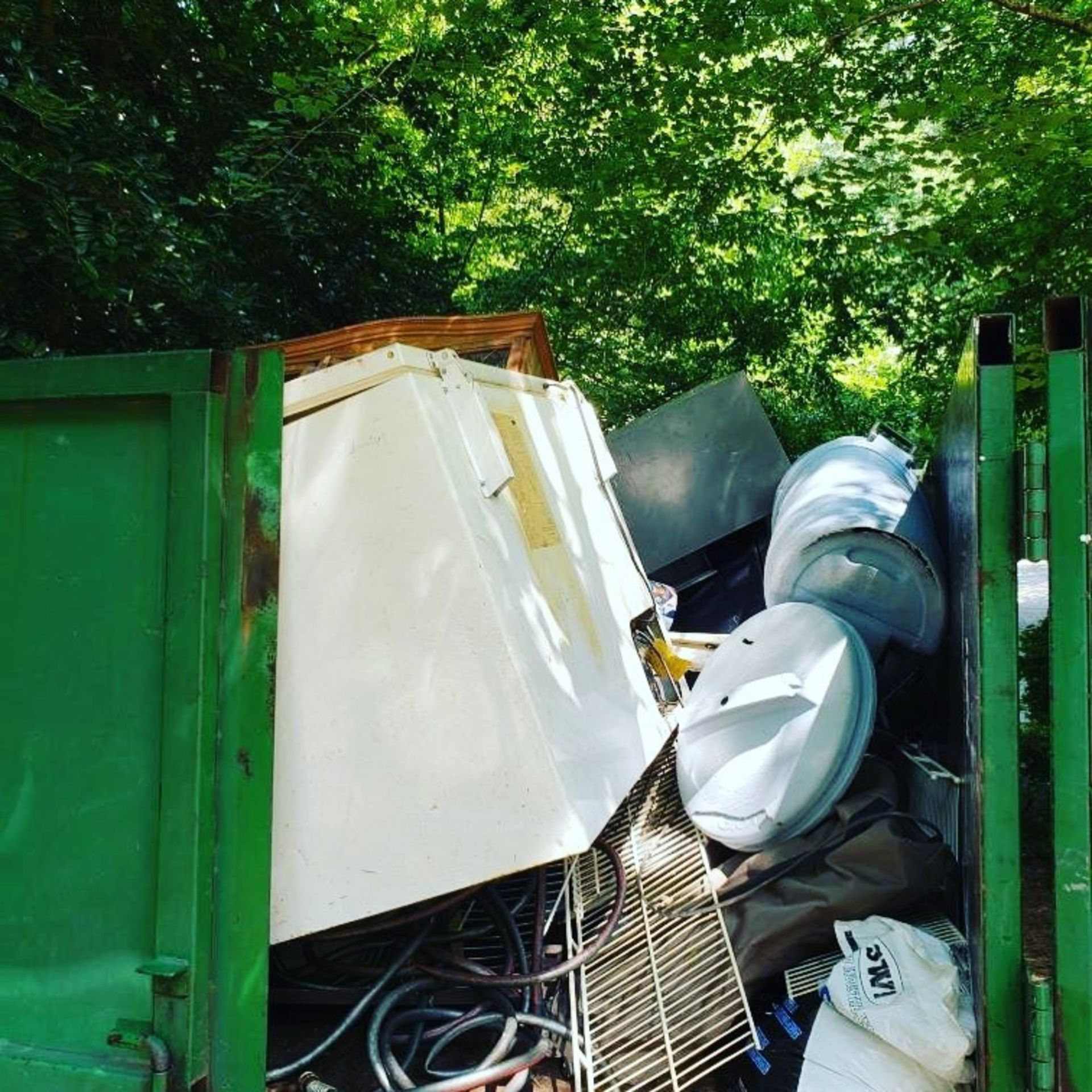 A green dumpster filled with junk including a white fridge.